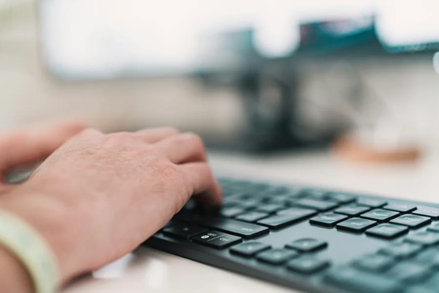 A close-up of a person's hand typing on a black computer keyboard with a blurred background.