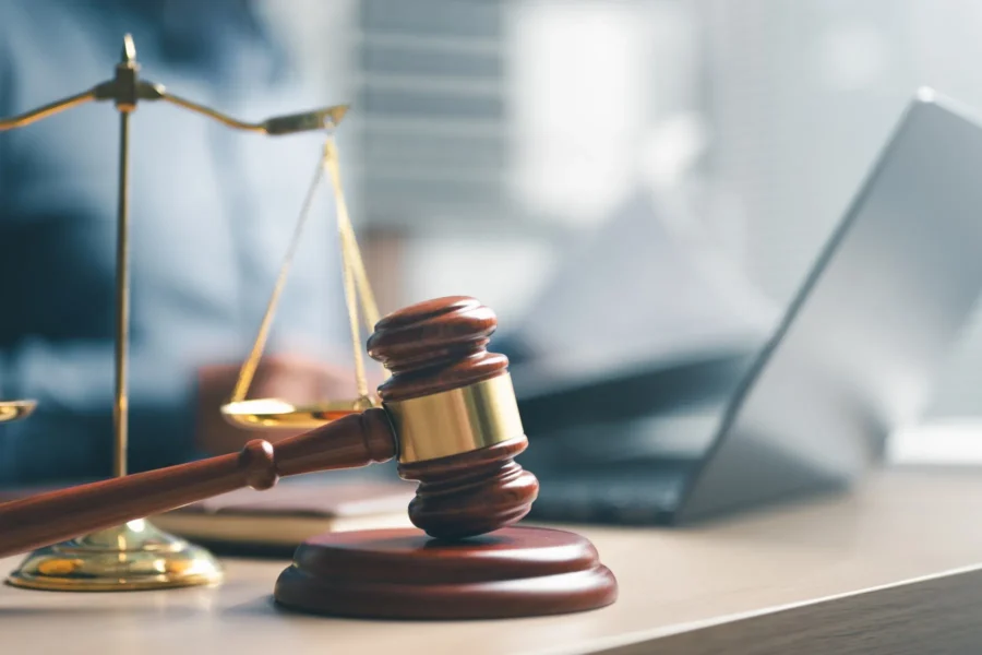 A judge’s gavel, a balance scale, and a laptop on a desk represent legal proceedings and judicial work.