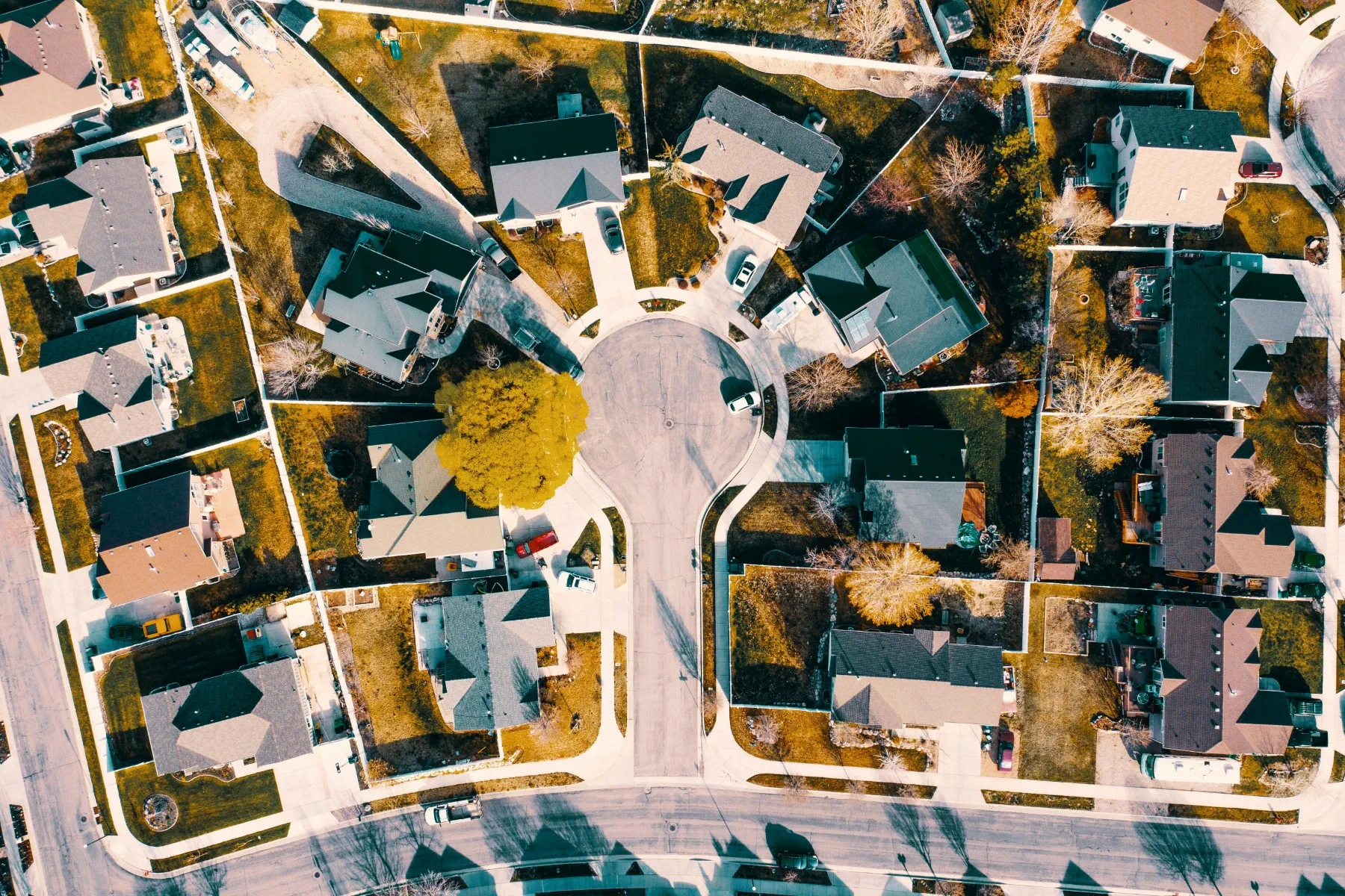 Aerial view of a suburban neighborhood cul-de-sac with houses, driveways, cars, and lawns visible, surrounded by streets and trees.