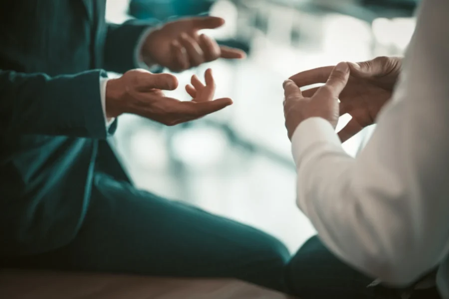 Two people in business attire engaged in a conversation, shown only from the waist up with focus on their expressive hand gestures.