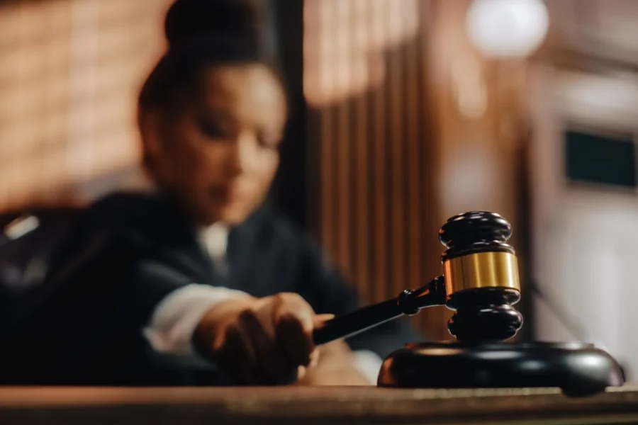 A judge holds a gavel and prepares to strike it on a sound block in a courtroom.