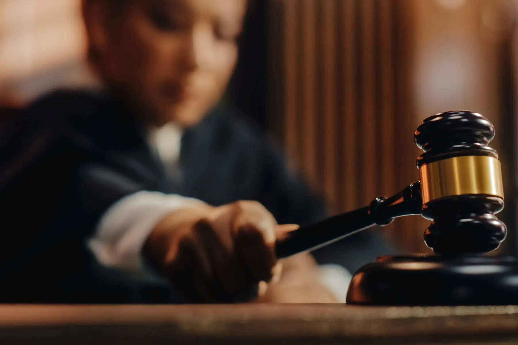A judge in a robe holds a gavel and prepares to strike it on a sound block in a courtroom.