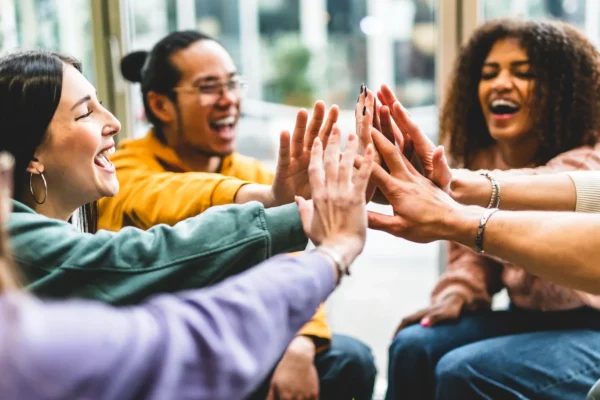 A group of people sitting in a circle, smiling and laughing as they reach out to high-five each other in the center.