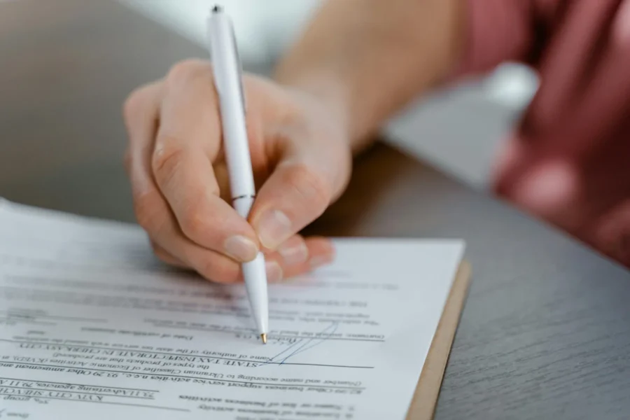 A person holding a pen signs a printed document on a clipboard placed on a table.