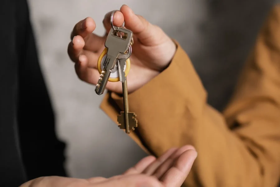 A person in a tan sleeve hands over a set of keys to another person with an open hand.