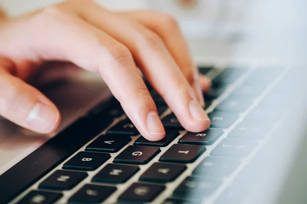 A person’s hand typing on a black computer keyboard.