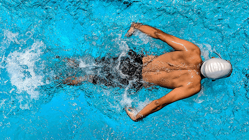 Man in a silver swim cap swimming in a pool at a fitness club